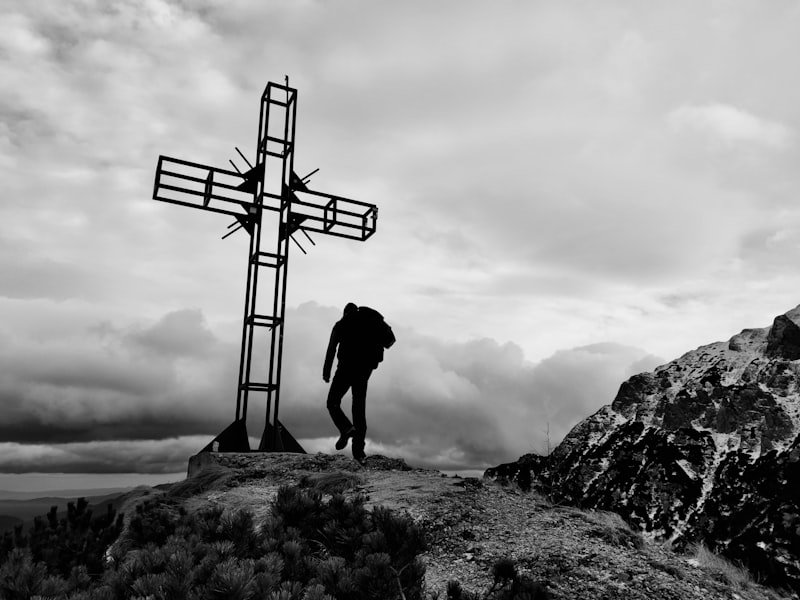 a man standing on top of a mountain next to a cross