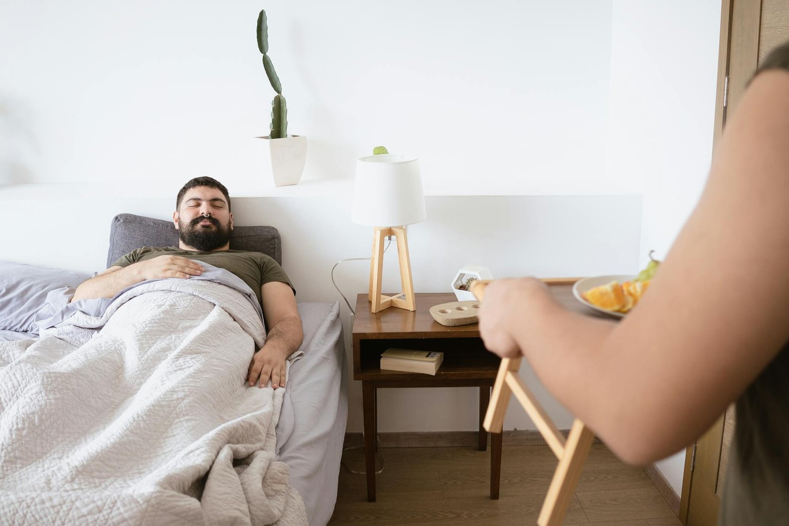 A man enjoys a relaxing morning as his partner brings breakfast in bed, creating a cozy and loving atmosphere.
