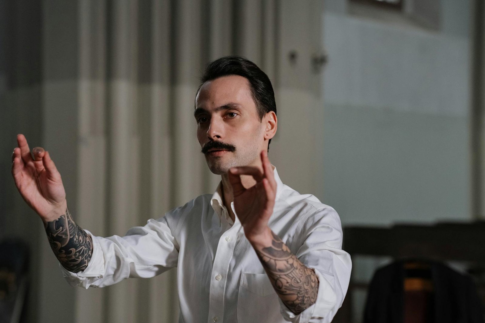 Tattooed conductor passionately leading a musical performance indoors.