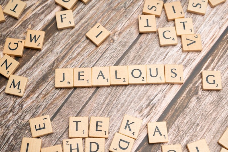 scrabble tiles spelling the word jellous on a wooden surface