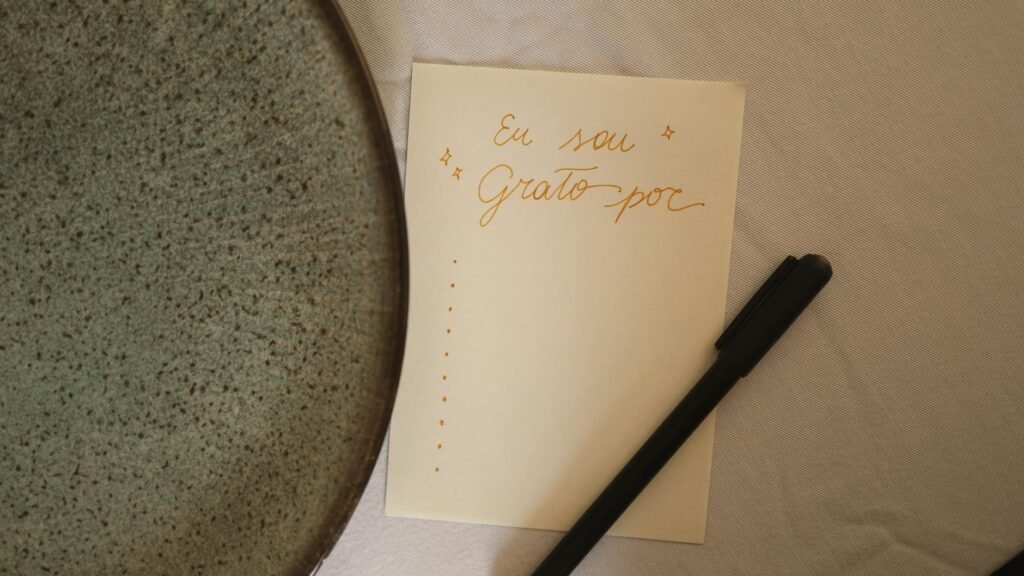 A note in Portuguese showing gratitude, accompanied by a pen and plate, on a table.