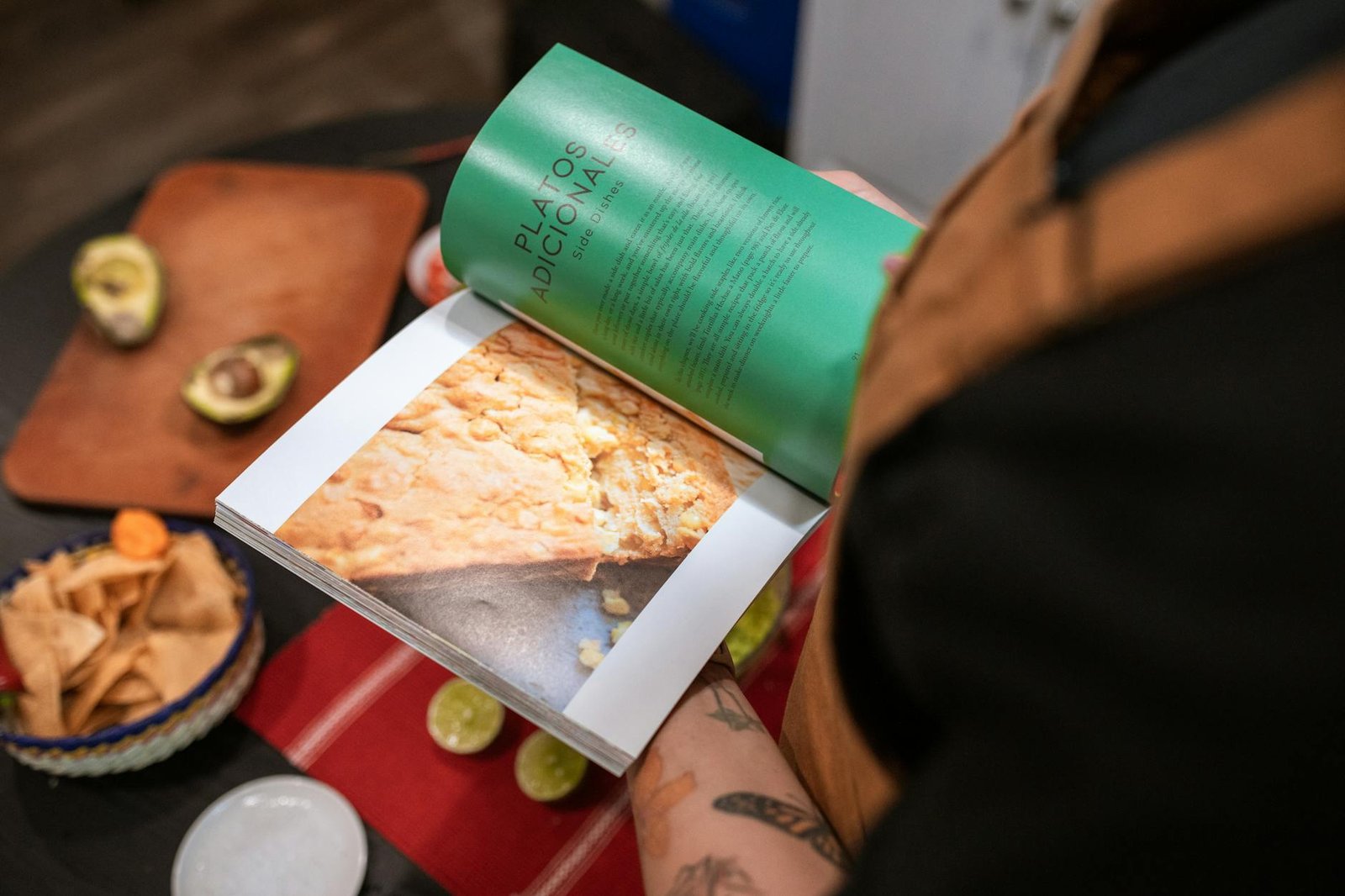 A close-up of a person using a cookbook in a kitchen, surrounded by ingredients.