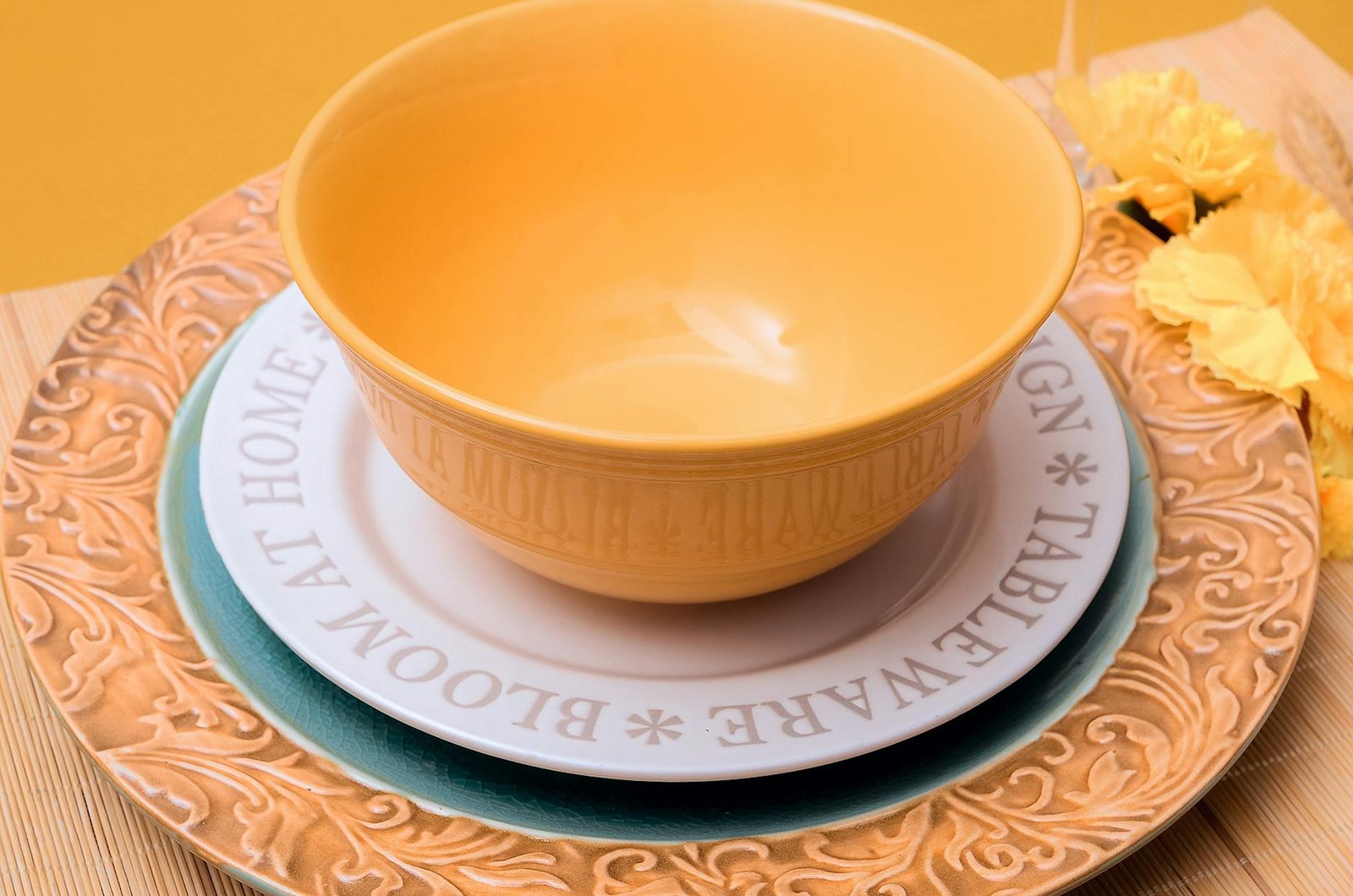 Artistic presentation of a yellow ceramic bowl set on a detailed decorative plate with autumnal floral accents.