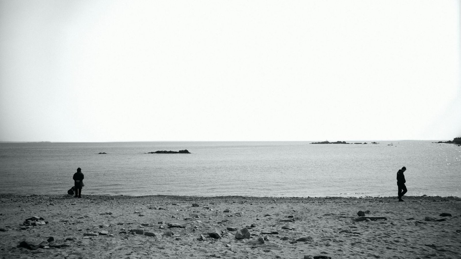 Black and white minimalist photo of a beach in Qingdao with two figures by the sea.