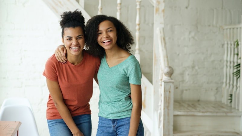 Two smiling young women standing together indoors.