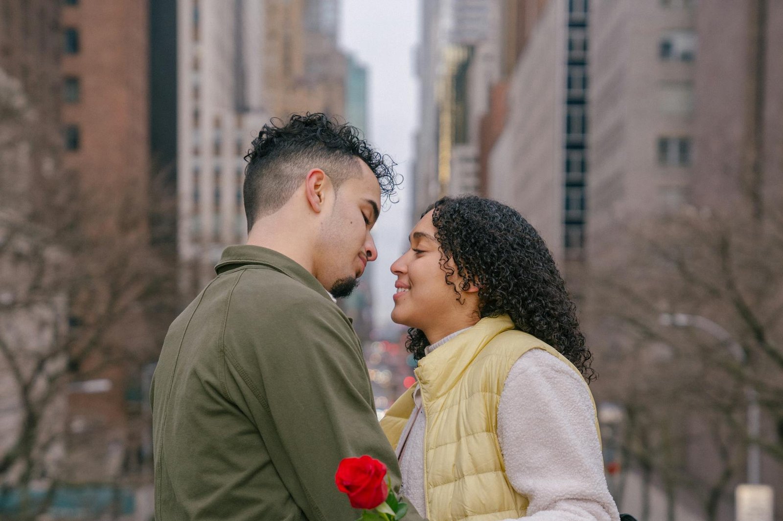 Happy couple sharing a romantic moment with a red rose in an urban city background.