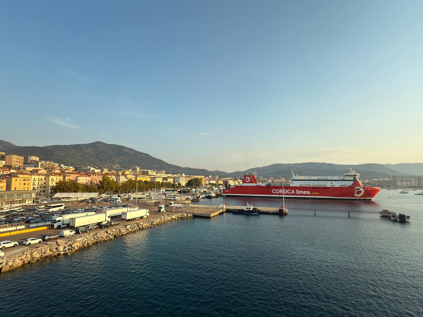 Scenic view of a ferry at Ajaccio port in Corsica, France with a mountainous backdrop and clear skies.