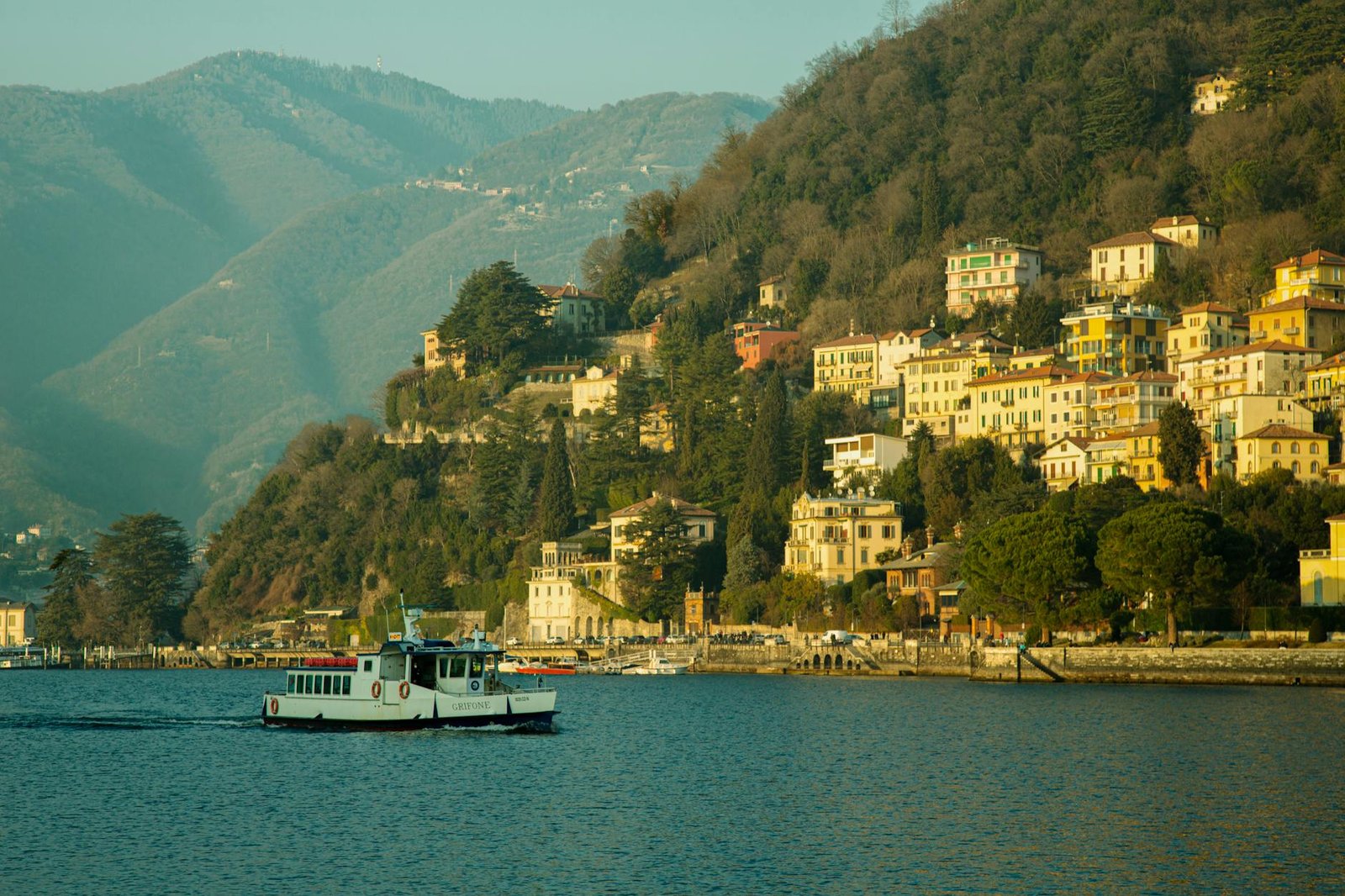 Picturesque view of Lago di Como with colorful hillside houses and a ferry in spring.