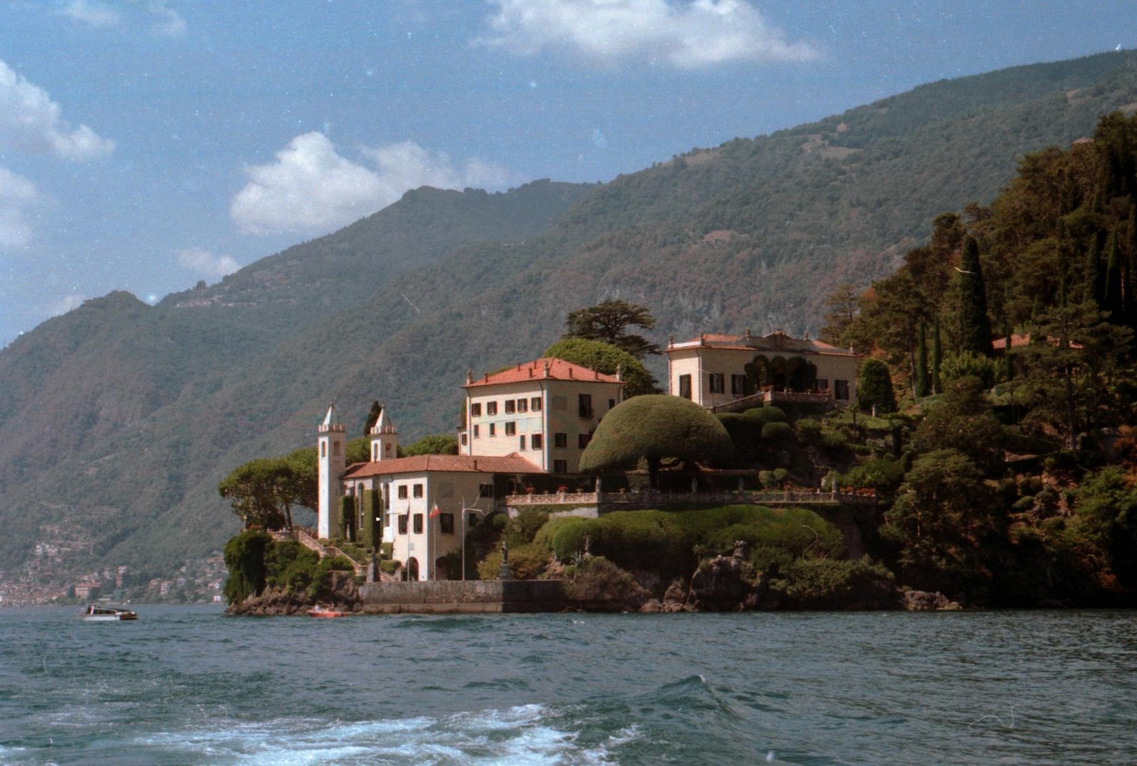 Picturesque view of a villa by Lake Como, Italy, nestled against lush hills under a sunny sky.