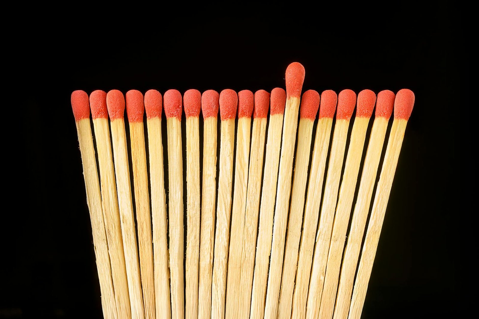 Close-up of red-tipped matchsticks on black backdrop, highlighting uniqueness.
