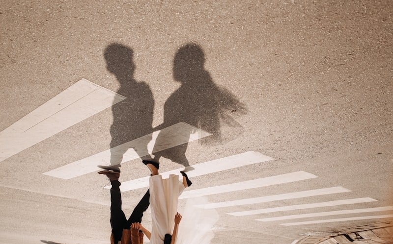 person in white long sleeve shirt and black pants walking on gray concrete pavement