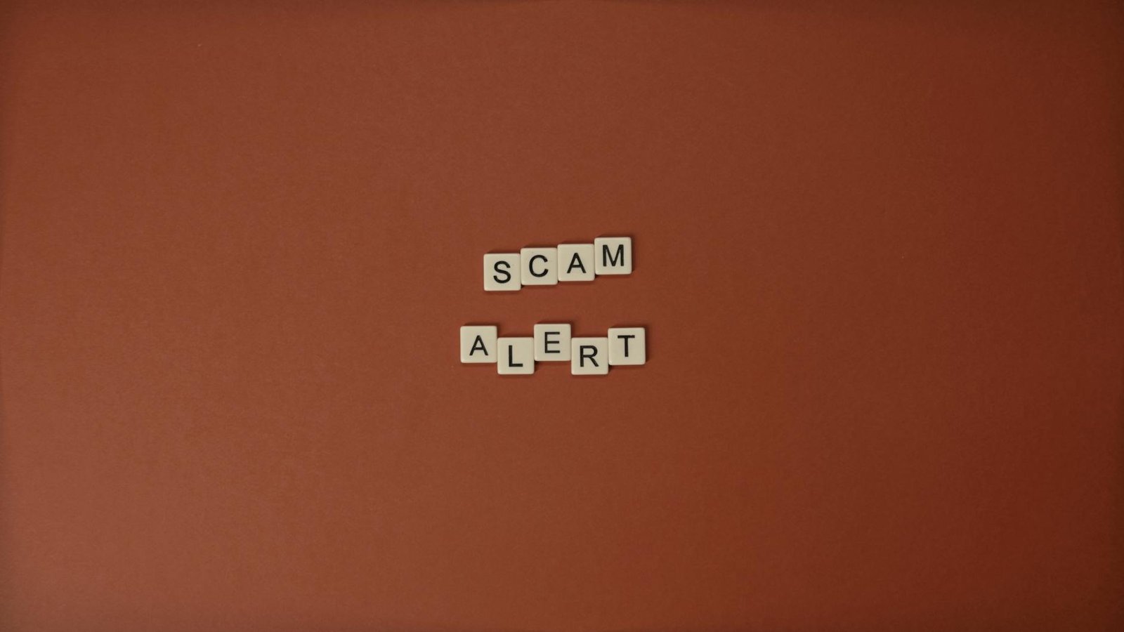 Scrabble tiles spelling Scam Alert on a brown surface indicating caution.