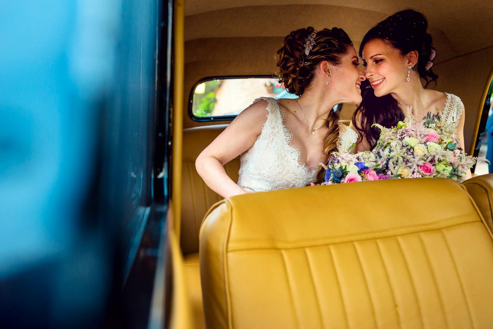 Joyful same-sex couple sharing a moment in a vintage car on their wedding day.