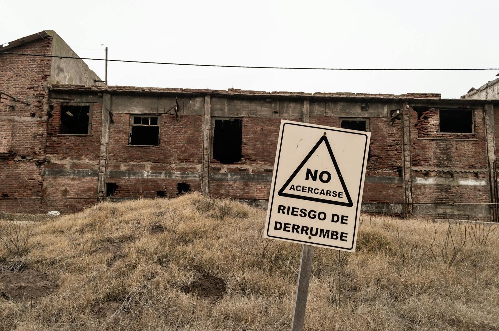 An abandoned brick building with a warning sign indicating risk of collapse in Spanish.