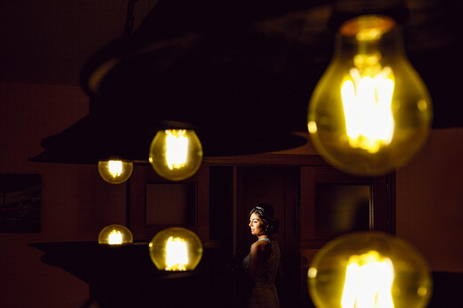 A bride poses elegantly in dramatic lighting surrounded by glowing bulbs, creating a unique wedding portrait.