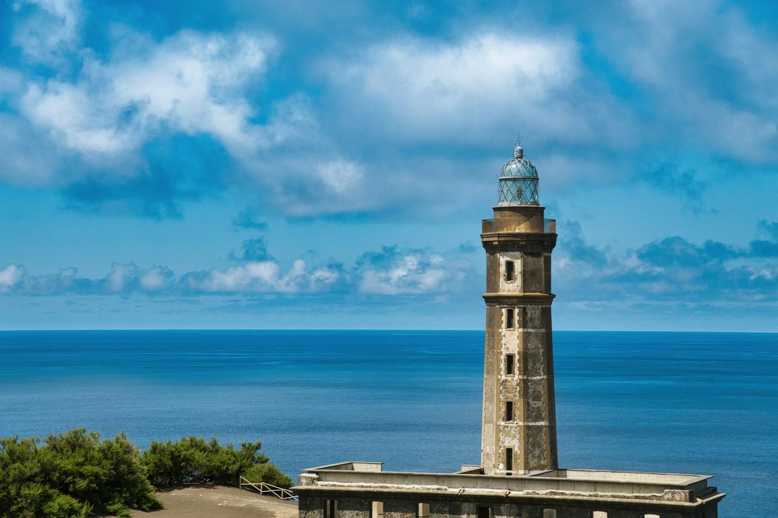 Historic lighthouse in Azores, Portugal, against a vibrant ocean and sky backdrop.