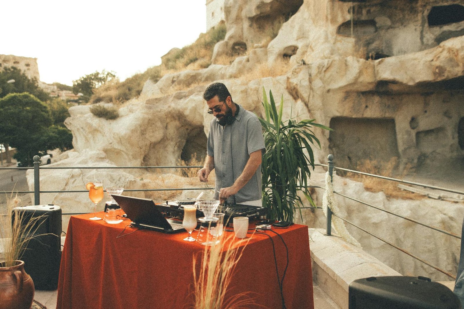 DJ mixing music outdoors on a terrace with rock formations. Vibrant and lively scene.