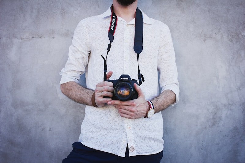 man in white dress shirt holding Canon DSLR camera