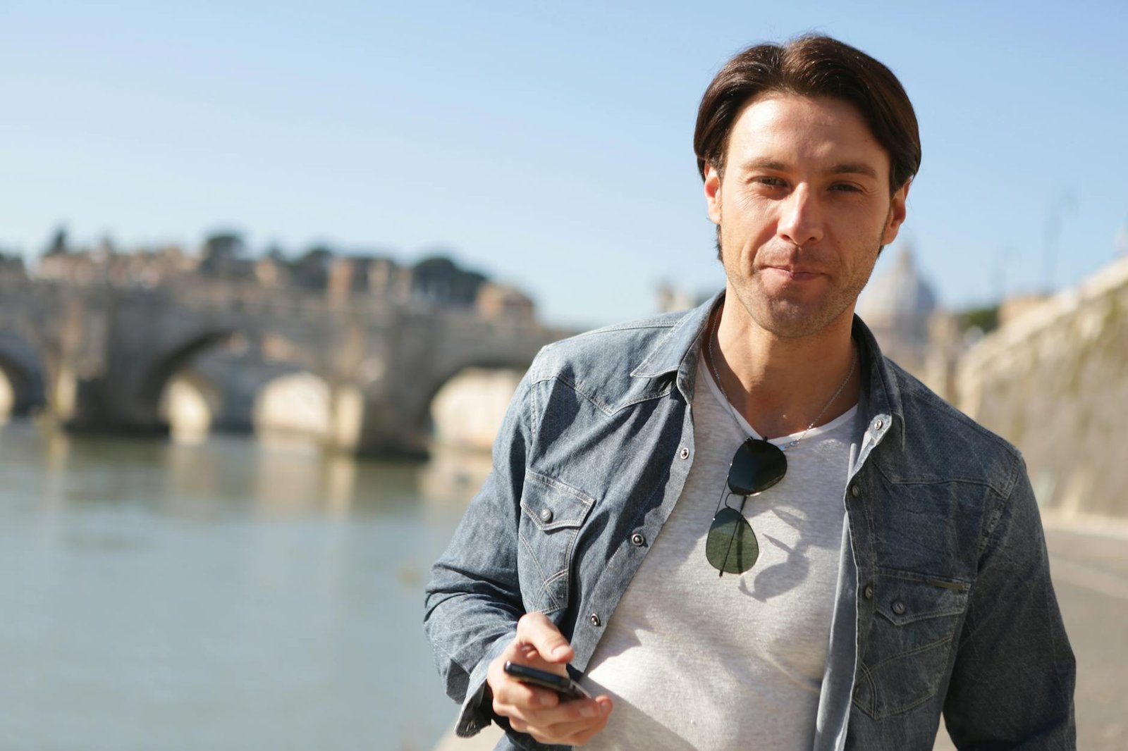Casual young man with smartphone standing by a scenic bridge by the water.