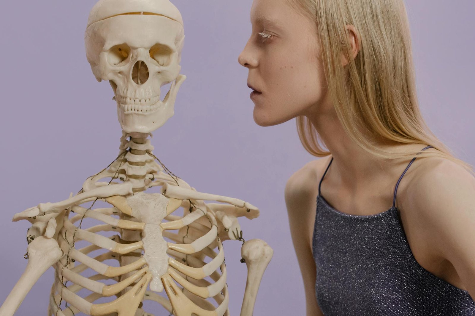 An artistic portrayal of a woman and skeleton against a purple background.