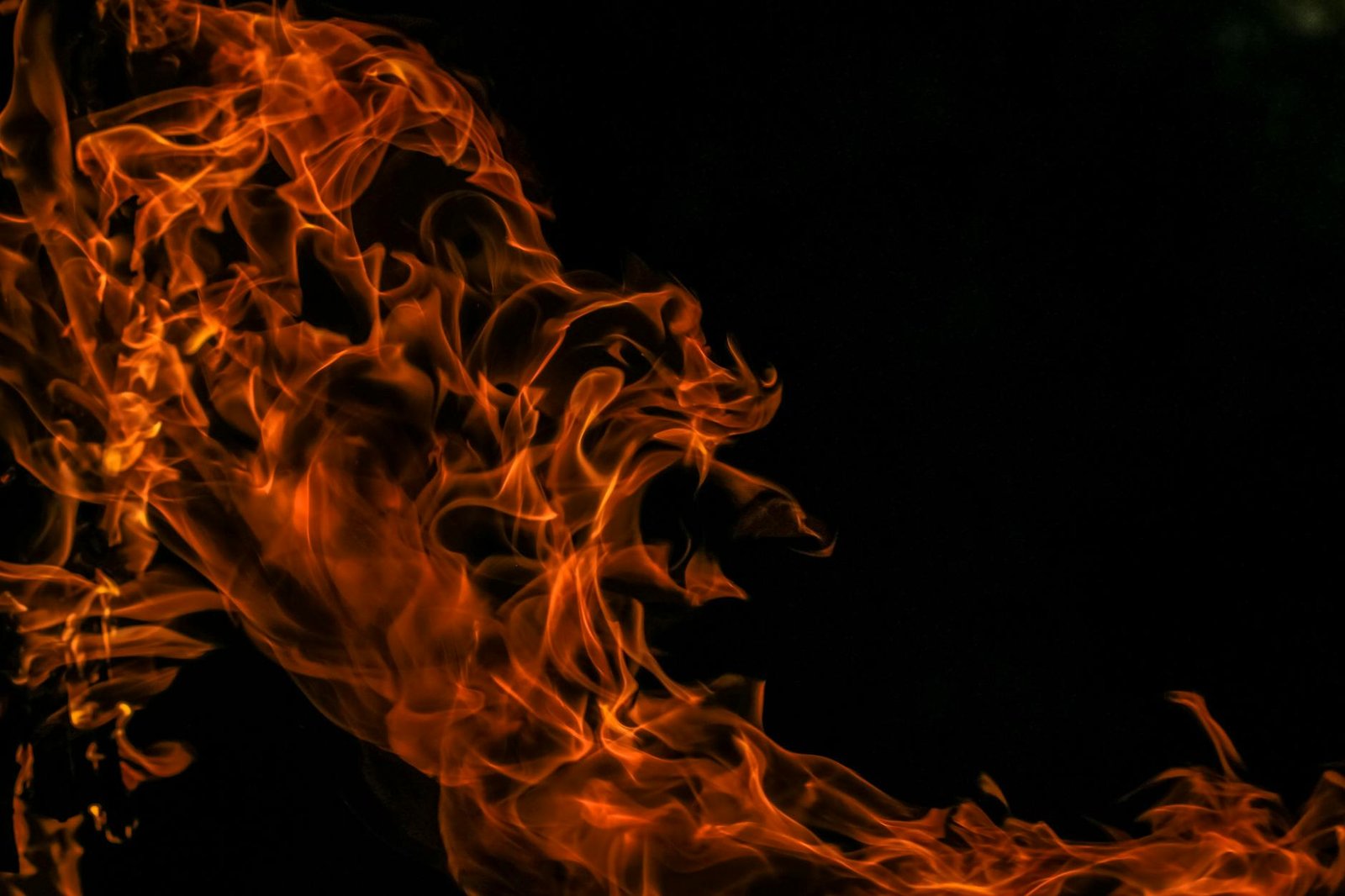 Close-up of vibrant orange flames dancing against a black backdrop, capturing the dynamic energy of fire.