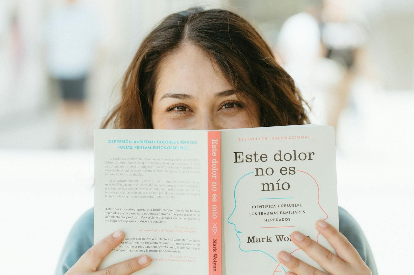 A woman enjoys reading a self-help book on emotional healing outside during the day.