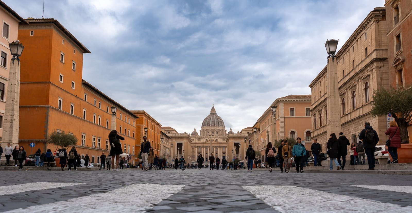 Crowds walking towards St. Peter's Basilica in the Vatican on a cloudy day.