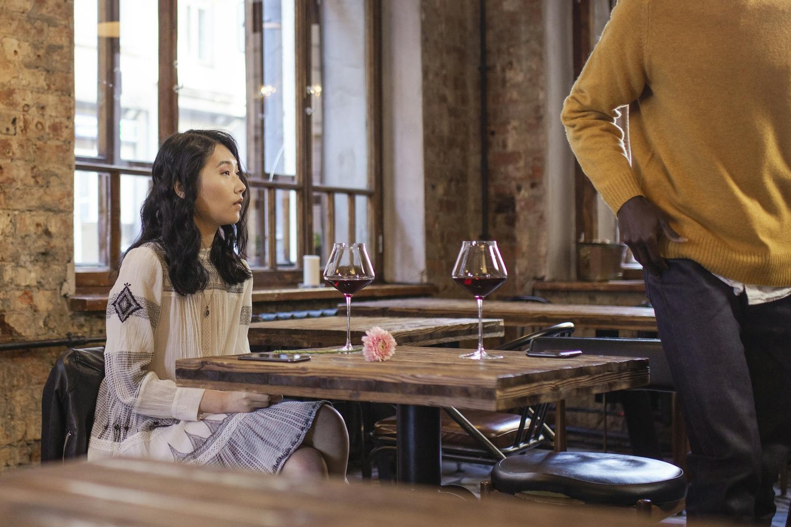 A woman seated at a café table with wine glasses, capturing a casual and warm ambiance.