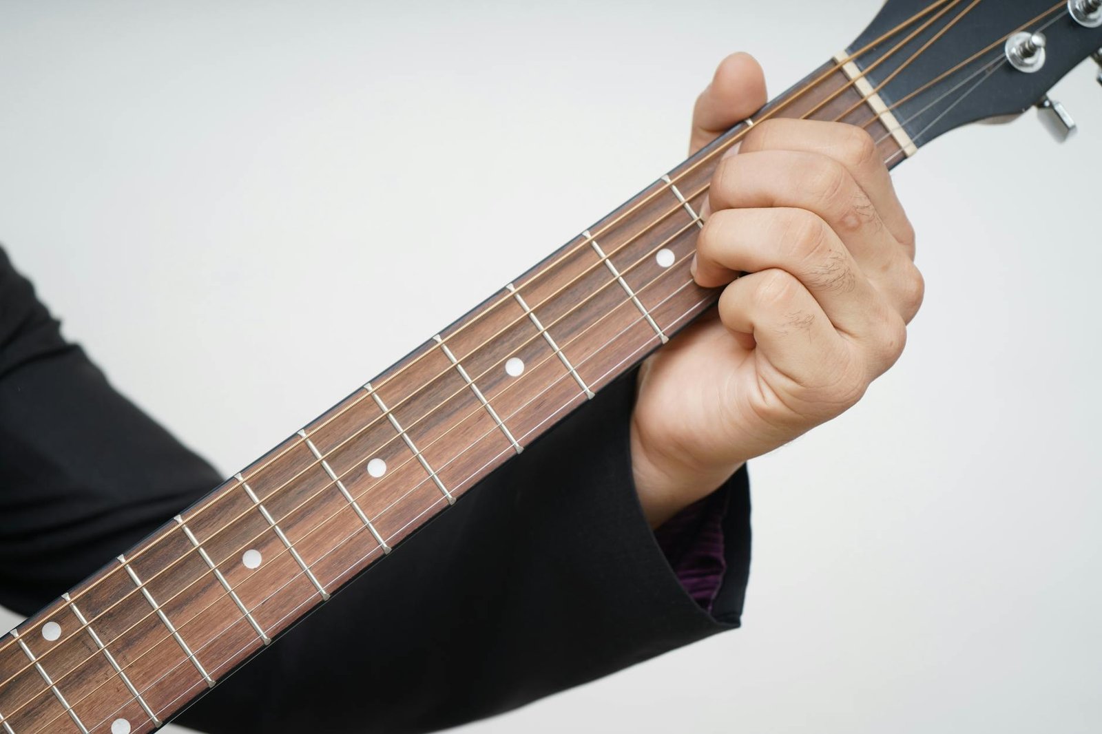 A detailed close-up of a hand playing a chord on an acoustic guitar neck.
