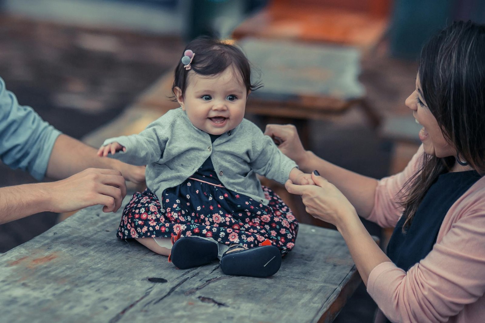 Adorable baby sitting on a table with parents holding hands indoors, smiling.