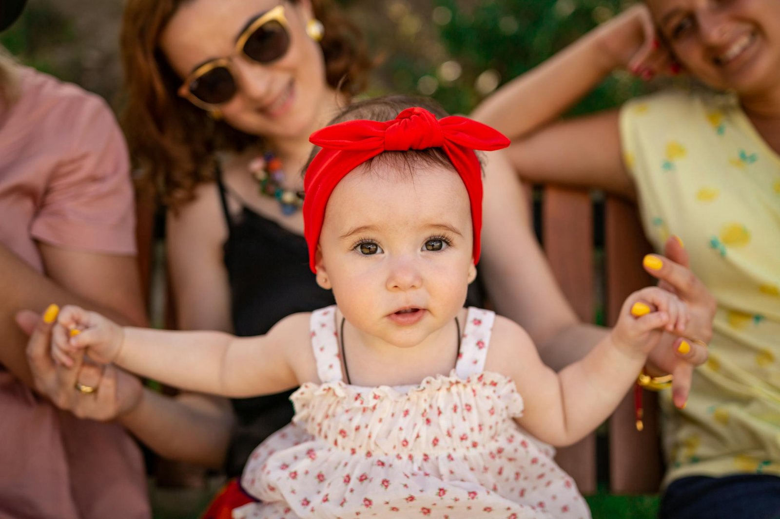 Charming baby girl with a red bow, enjoying a sunny day outdoors with family.