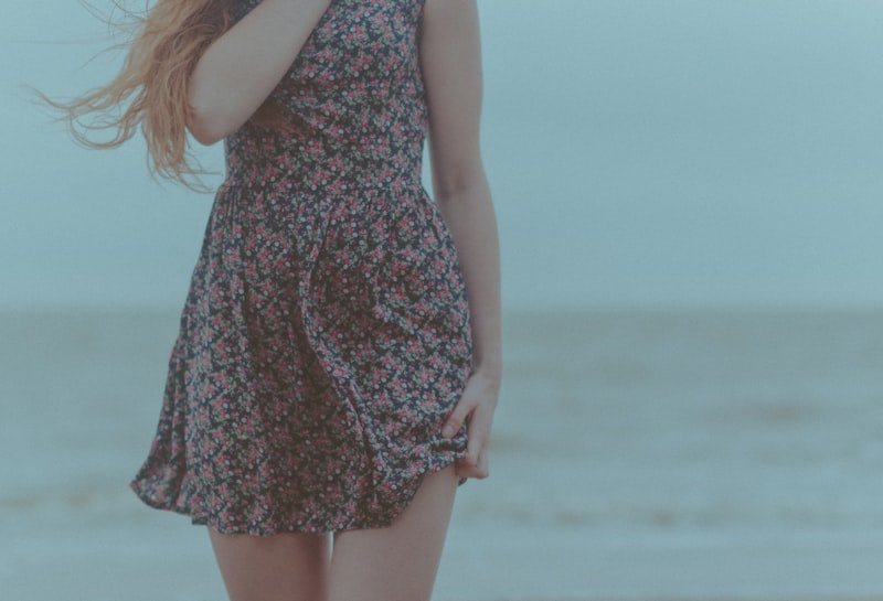 woman in blue and white floral sleeveless dress standing on beach during daytime