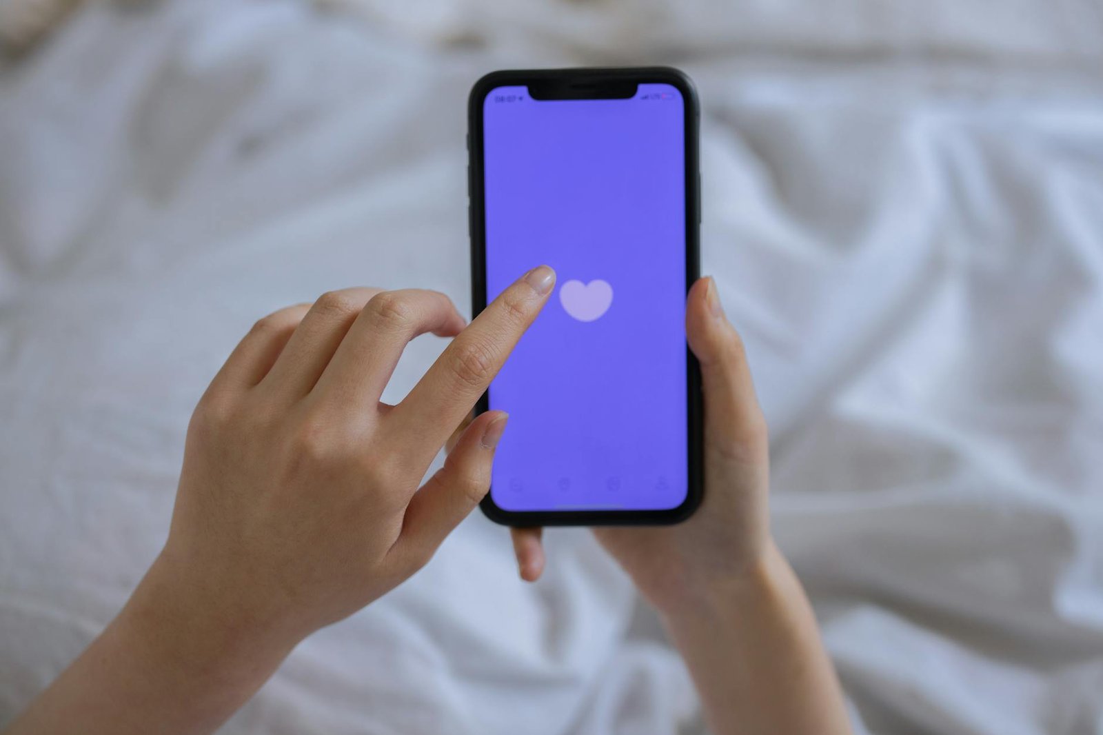 Close-up of hands using a smartphone with a heart icon on screen, representing technology and connection.