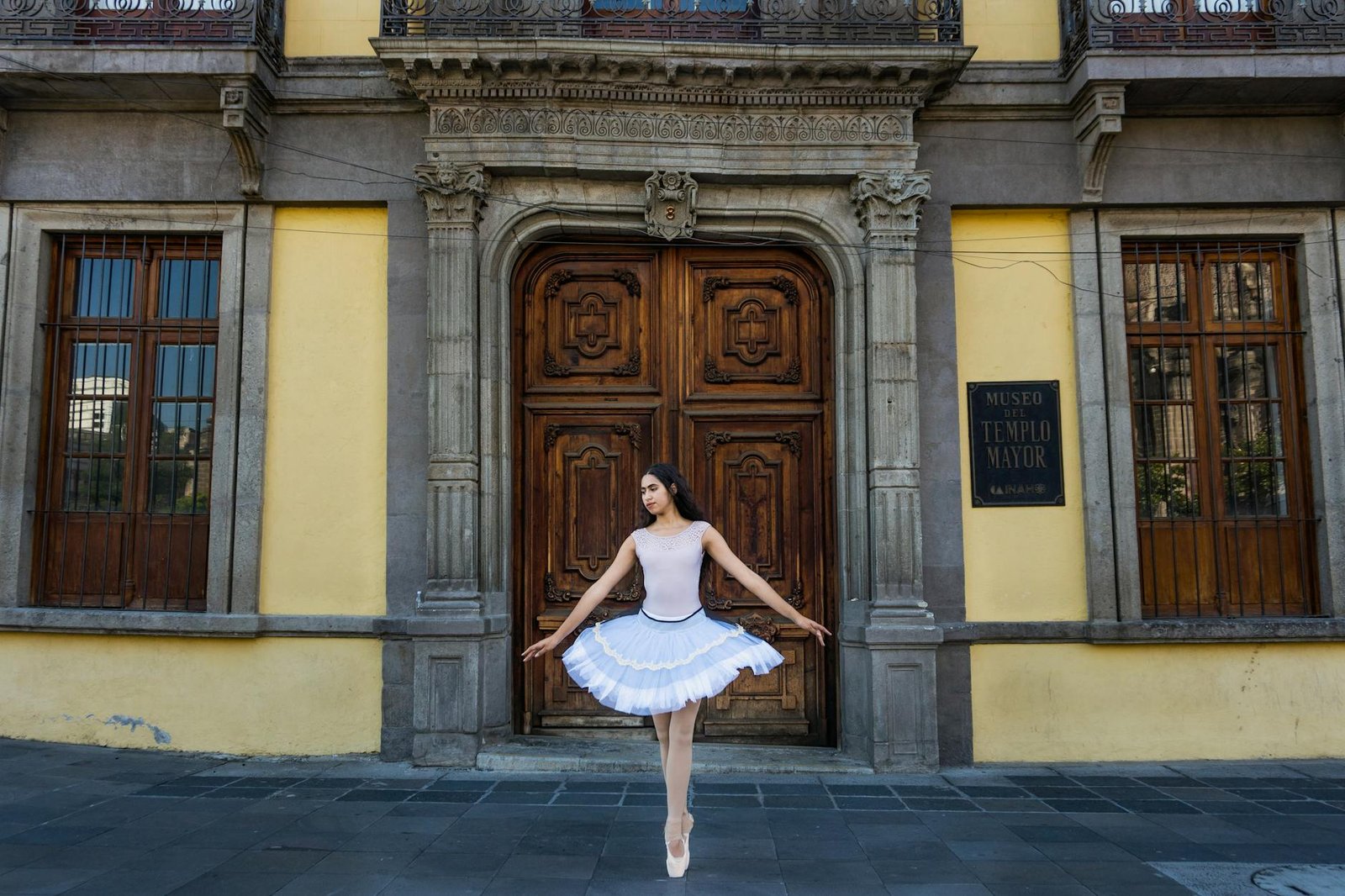 Ballet dancer elegantly poses outside historic building in Mexico City's urban landscape.