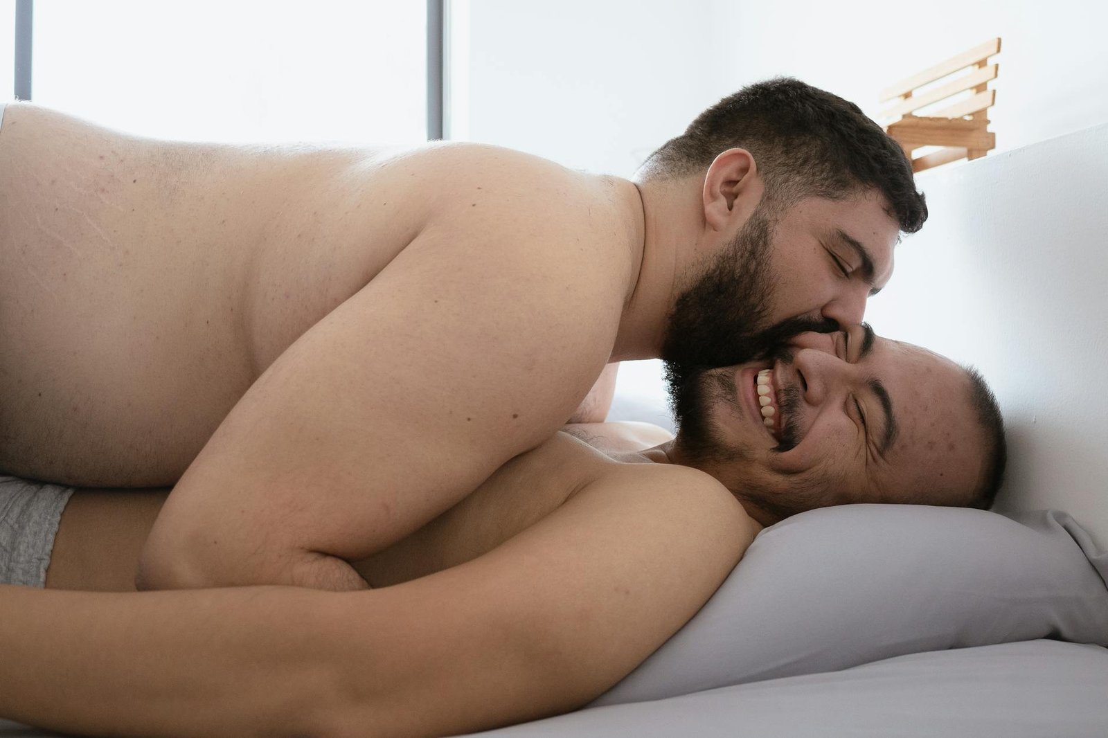 Joyful embrace of a gay couple in a bedroom, showcasing affection and love.