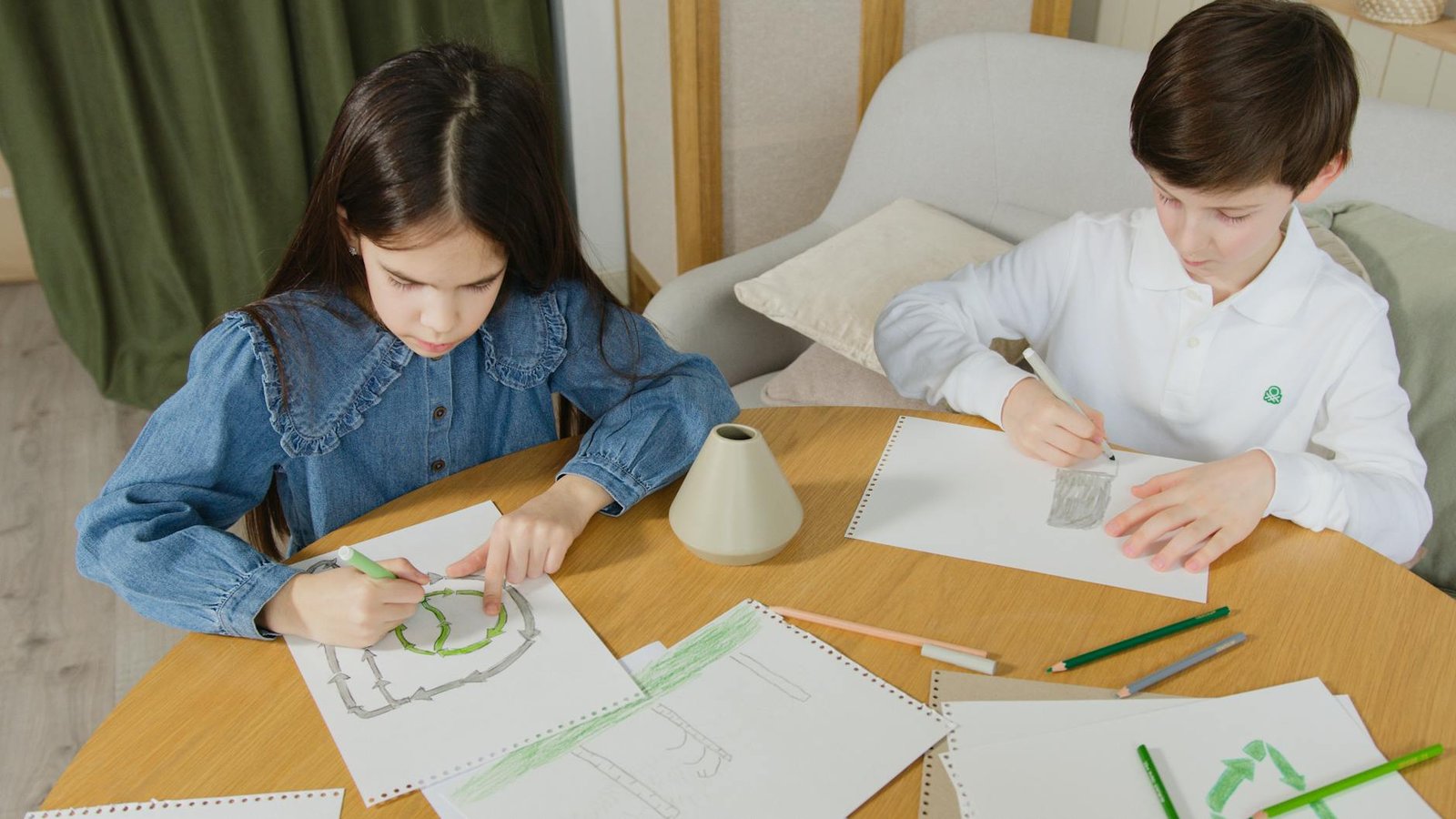 Two children enthusiastically drawing with pencils at a table indoors, focusing on their artwork.