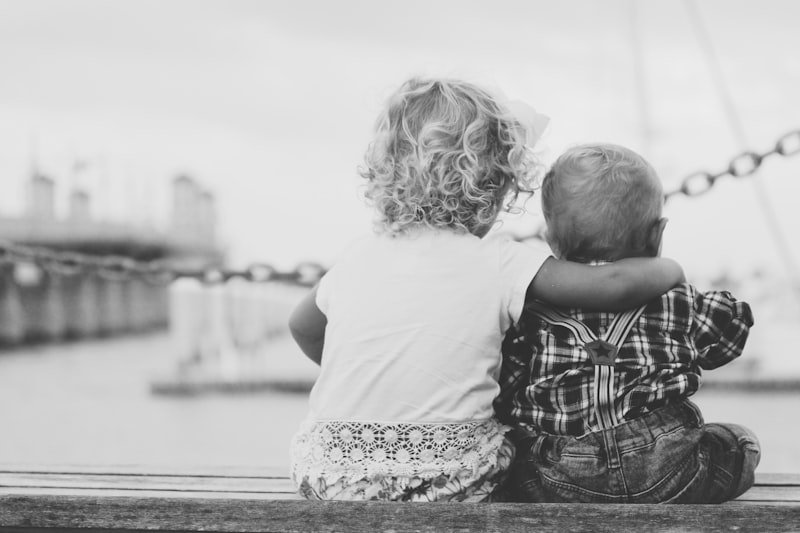 grayscale photography of two children sitting on ledge