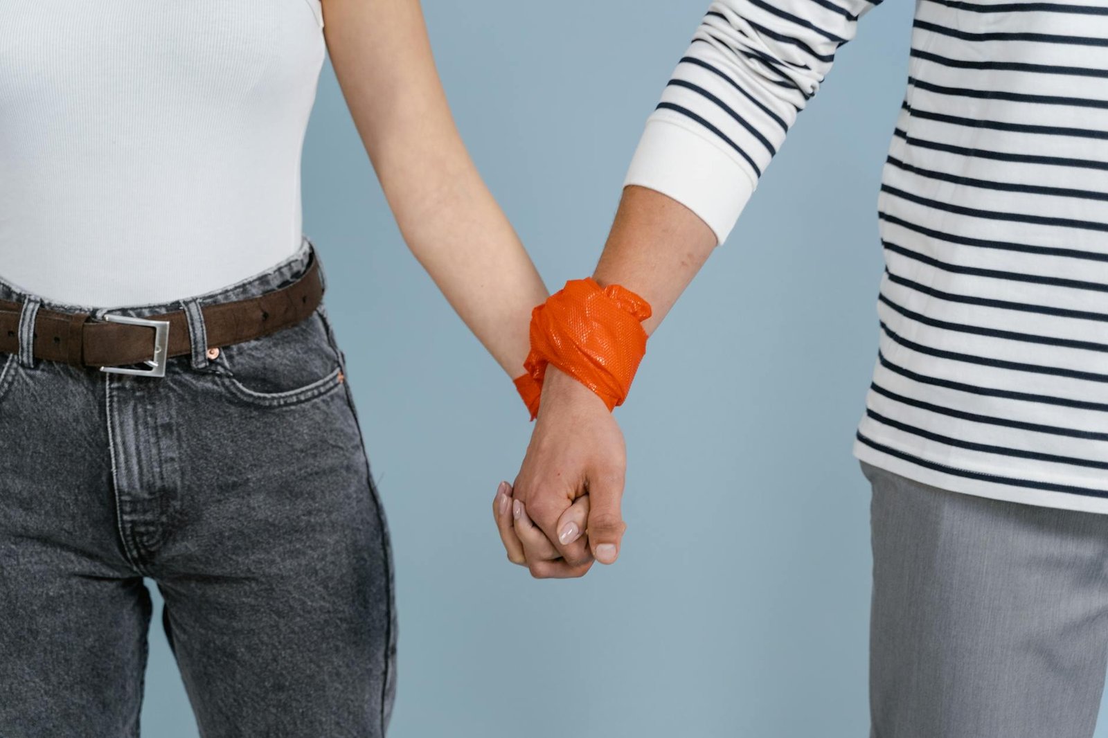 Close-up of a couple holding hands with an orange band on a blue background.
