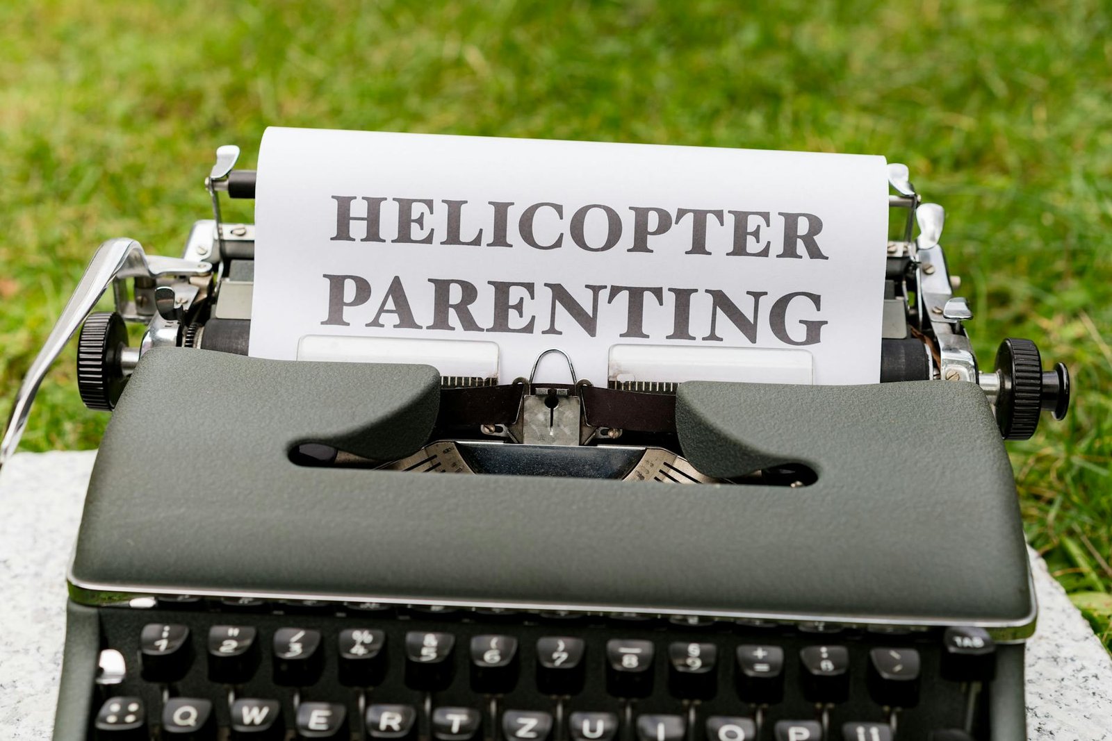 Close-up of a vintage typewriter outdoors with a paper displaying 'Helicopter Parenting'.