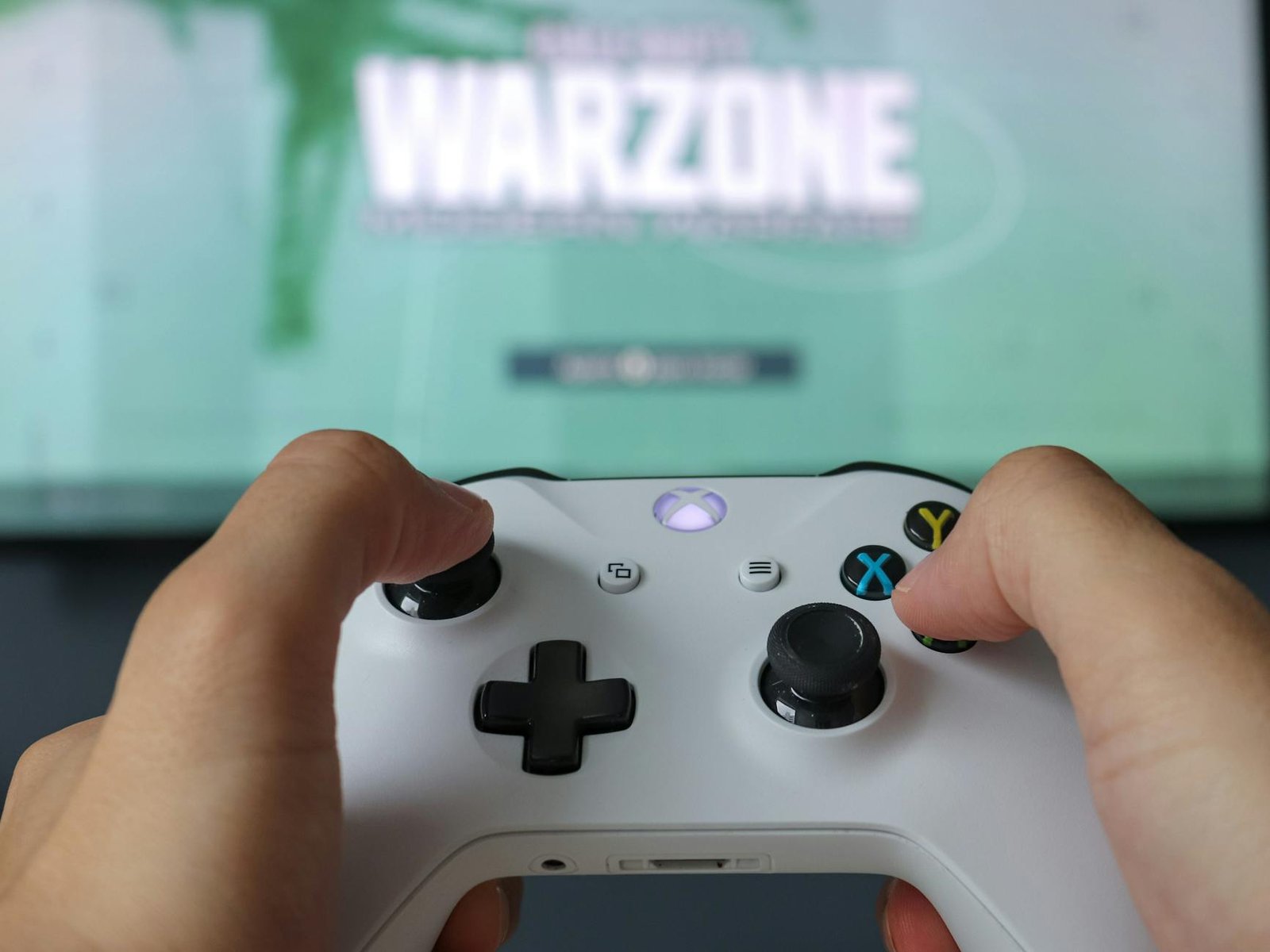 A close-up of hands holding an Xbox controller against a game screen, highlighting the gaming experience.