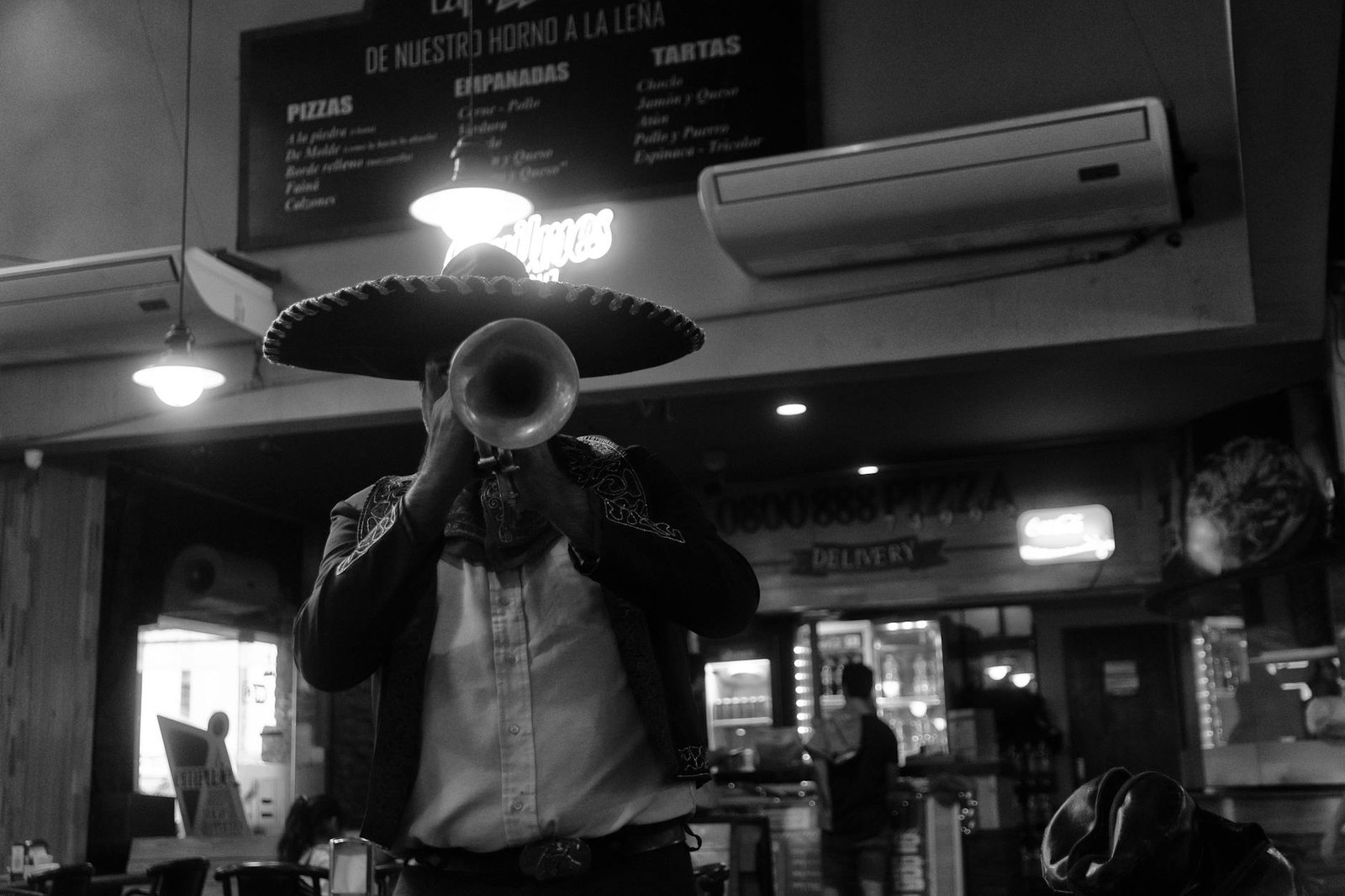 Black and white photo of a mariachi musician in a sombrero playing trumpet indoors.