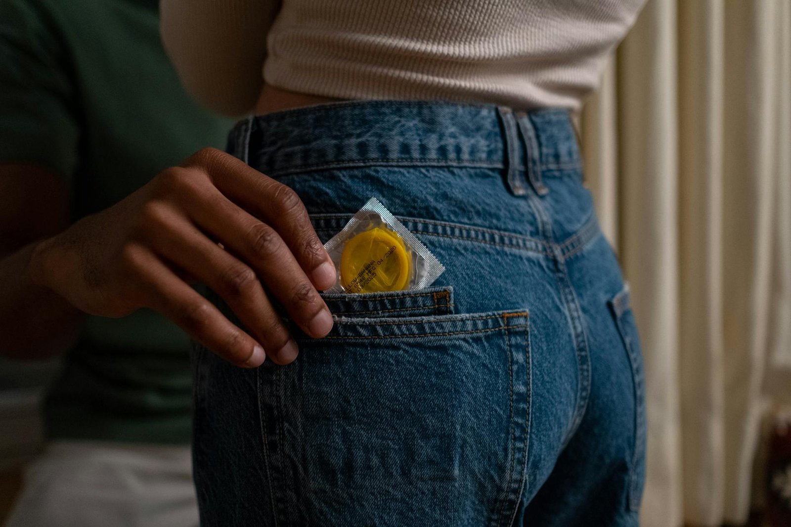 Condom being placed into denim jeans pocket, emphasizing safe sex and contraceptive use.