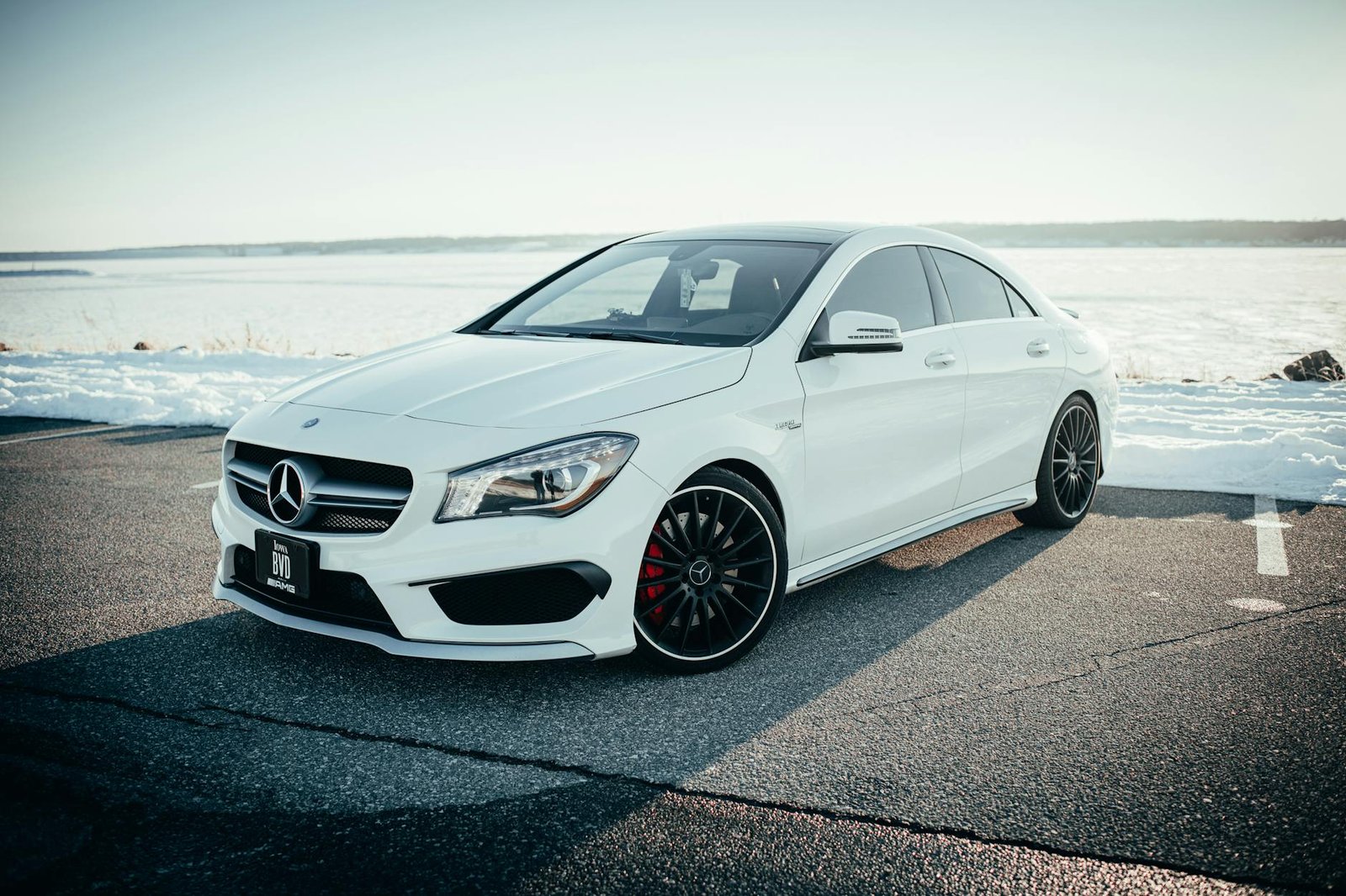 Sleek white Mercedes Benz sedan parked on a snowy road with a tranquil background.