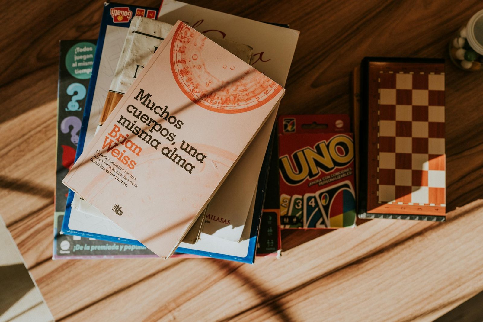 Top view of books, board games, and UNO cards in warm sunlight on a wooden table.