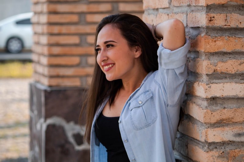 smiling woman leaning her back on brick wall